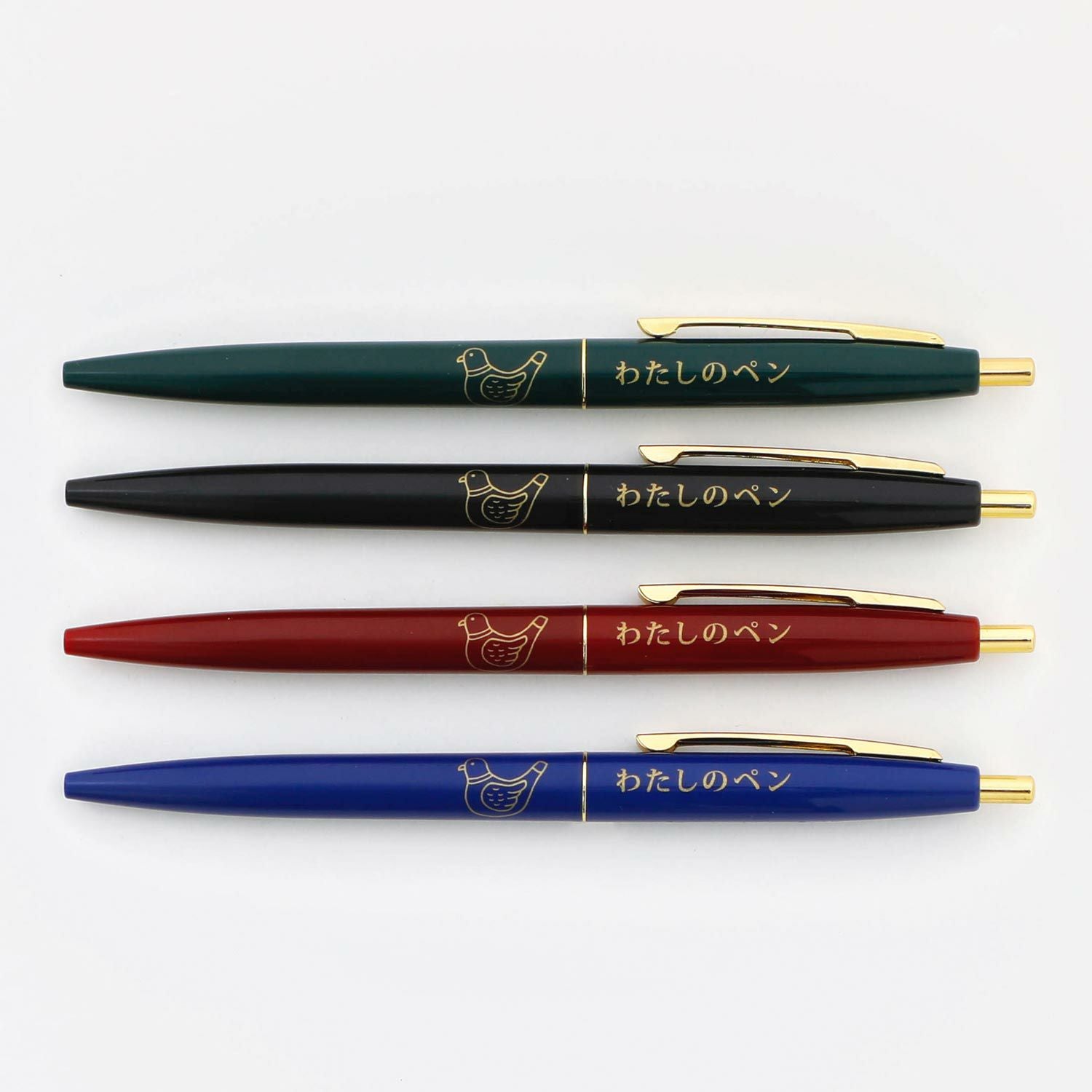 Four pens in green, black, red and blue lined up, showing gold pigeon and Japanese text.