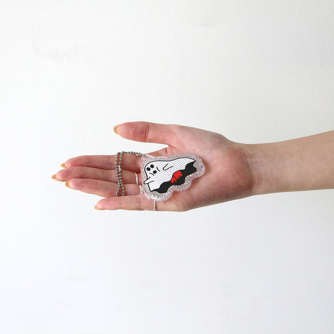 Open hand holding a ghost-shaped reflector keychain with red details on a ball chain, showing its small size.