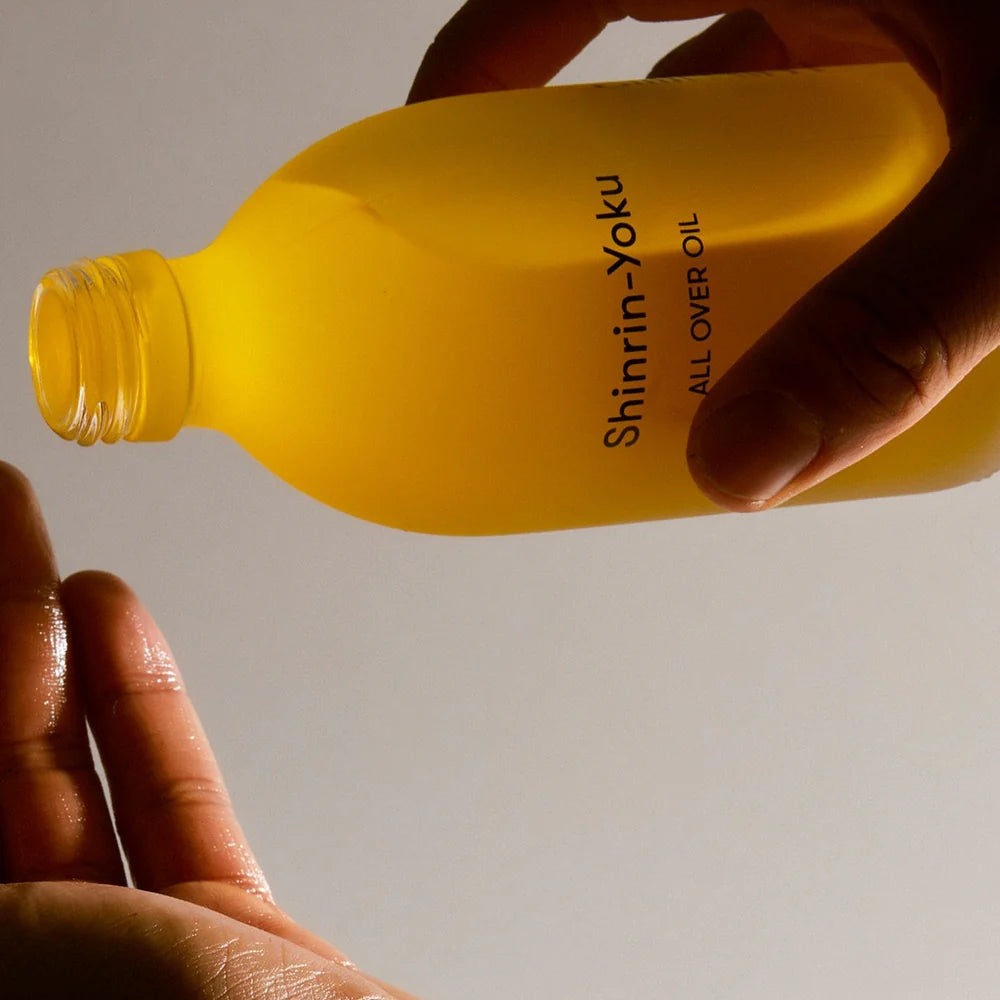 Hand tilting an open bottle of Earl of East Shinrin-Yoku All Over Oil above an oiled open palm.