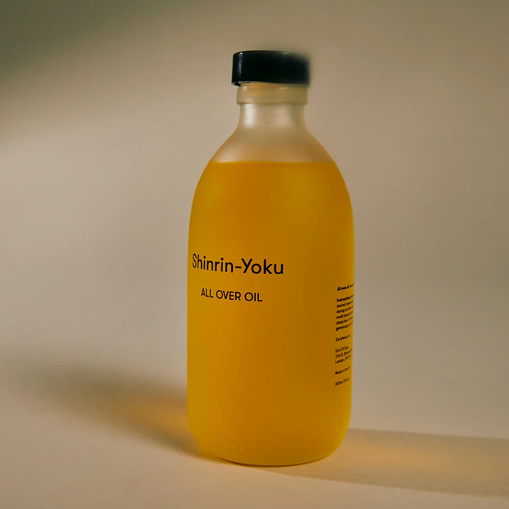 Glass bottle of Earl of East Shinrin-Yoku All Over Oil with black cap, golden oil and printed label.