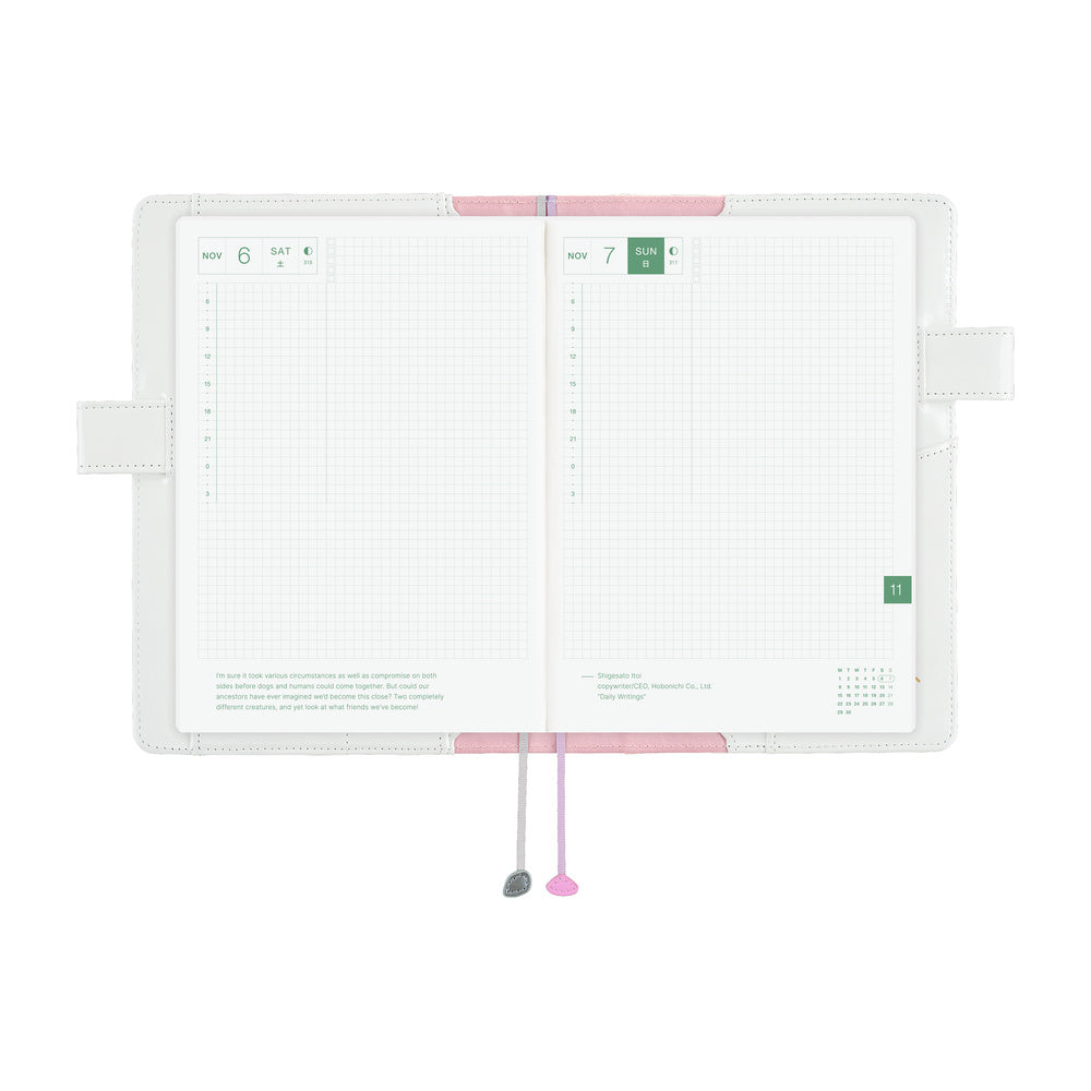 White A5 Cousin book cover opened flat, showing grid daily pages with pink lining and two ribbon markers.