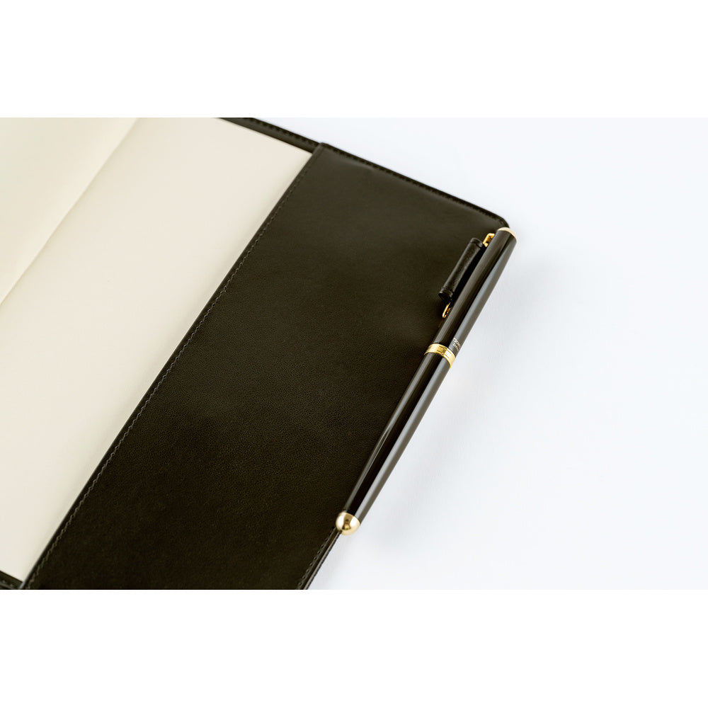 Close-up of an open Navy planner cover with a dark pen held in a side loop and plain pages inside.