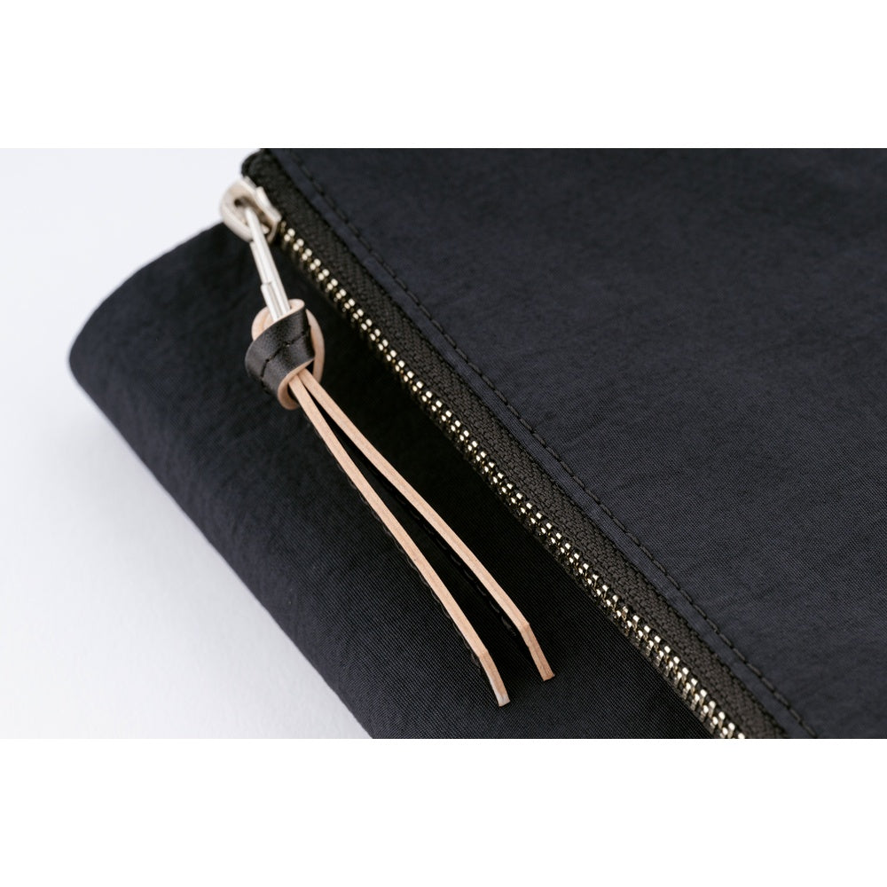 Close-up of a Black fabric book cover's metal zipper with leather pull tab and tan cord tassels.