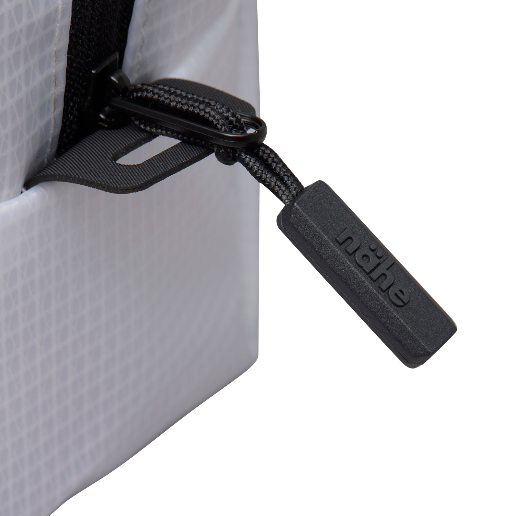 Close-up of the black zipper pull with embossed Nähe logo and cord on the Clear grid pouch.