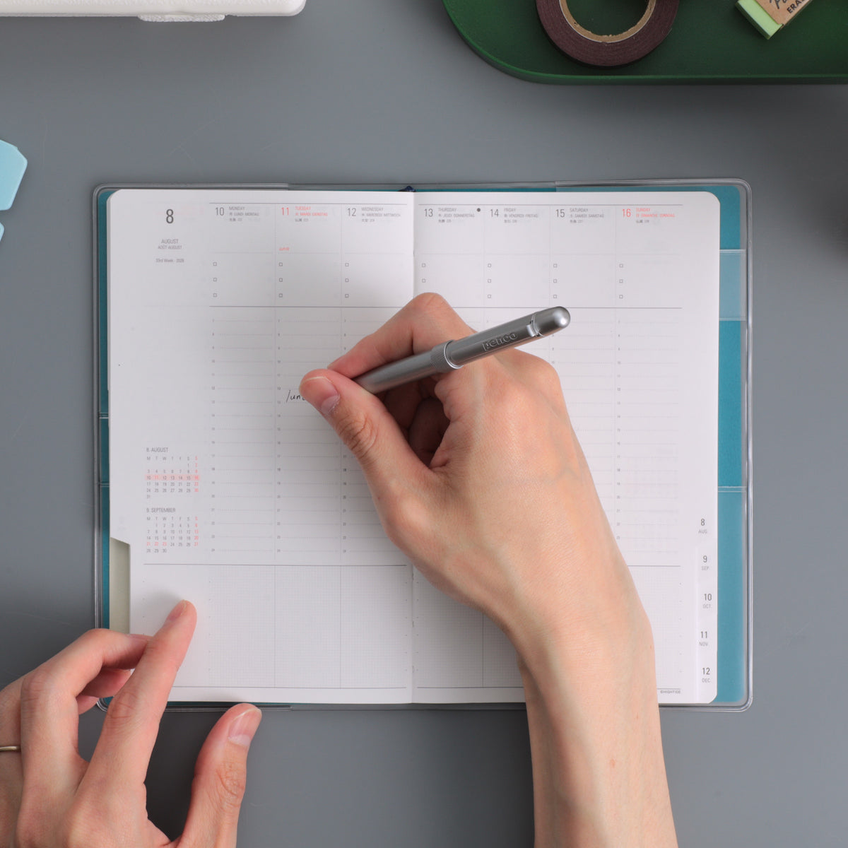 Hand writing with a silver pen in an open Nähe B6 Slim weekly planner with vertical time columns.
