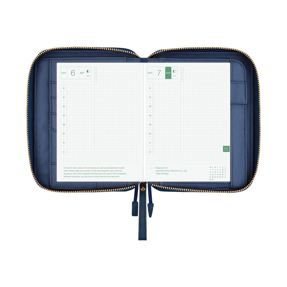 Open navy zip A6 planner cover showing grid daily pages, inner pockets and zipper pull tabs.