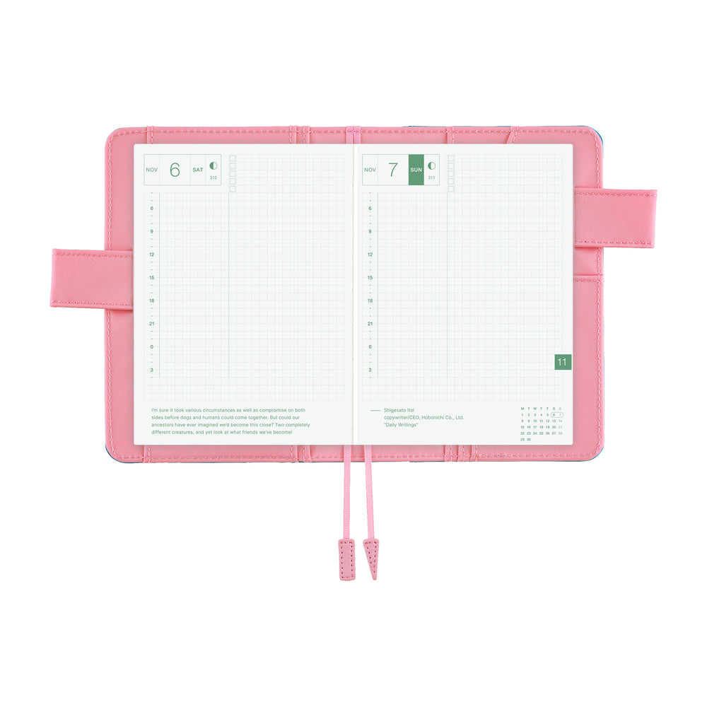 Pink Hobonichi A6 book cover opened flat, holding a daily planner with grid pages and two bookmarks.