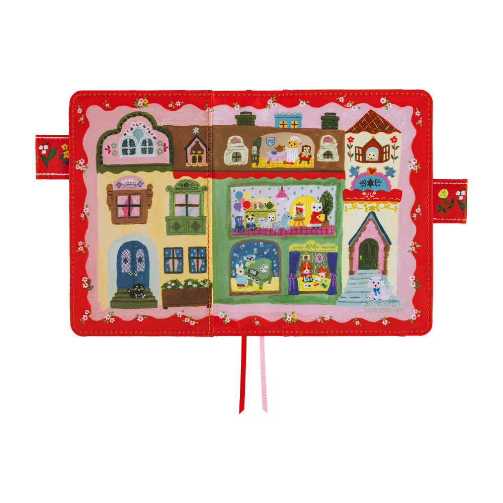 Red A6 planner cover opened flat, illustrated with storybook shops and animals, plus ribbon bookmarks.