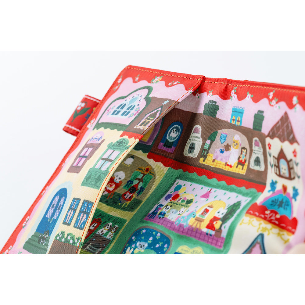 Close-up of a Red fabric book cover printed with a colorful illustrated dollhouse scene and stitched edge.
