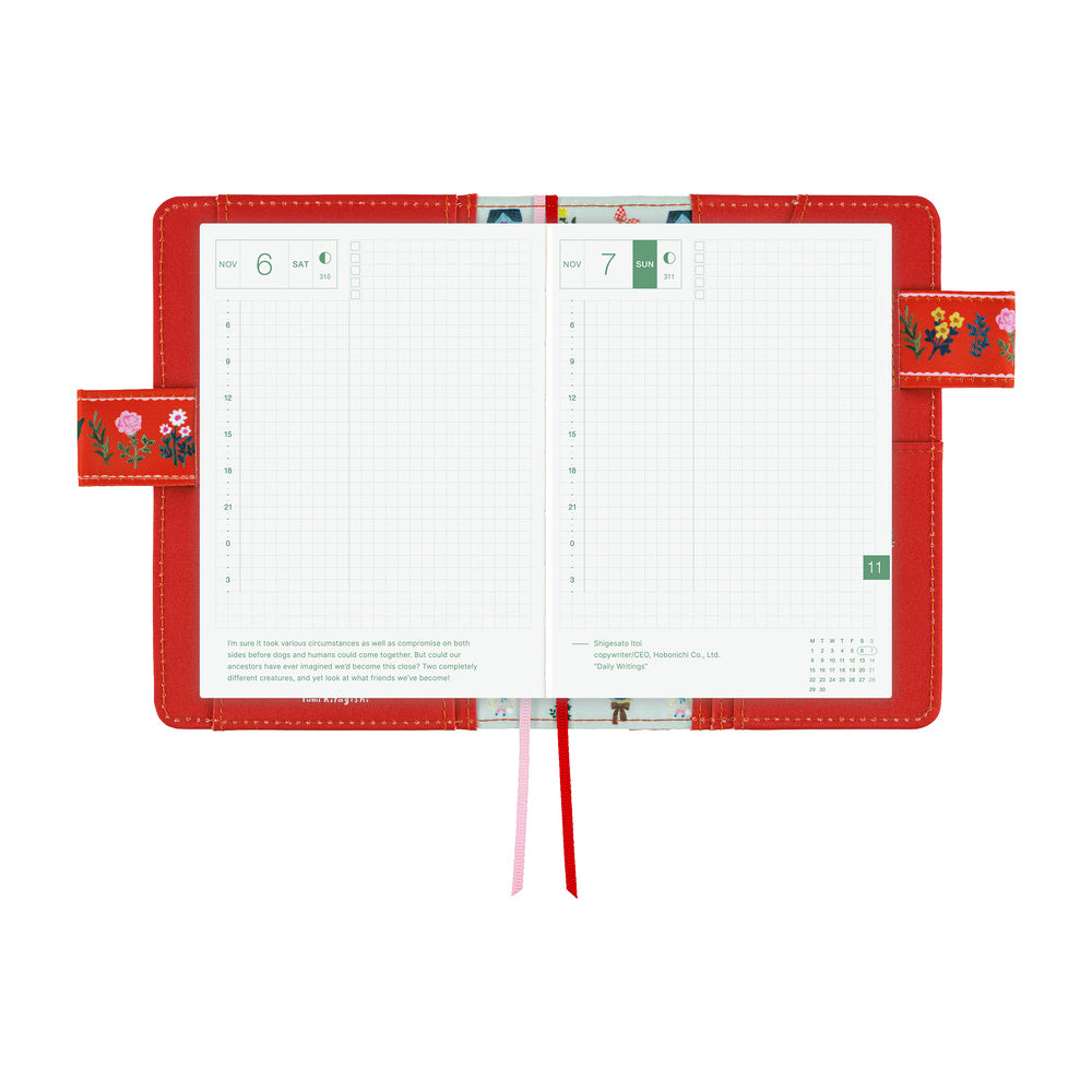 Red A6 book cover opened flat to show grid daily pages, floral-embroidered side flaps and two ribbon markers.