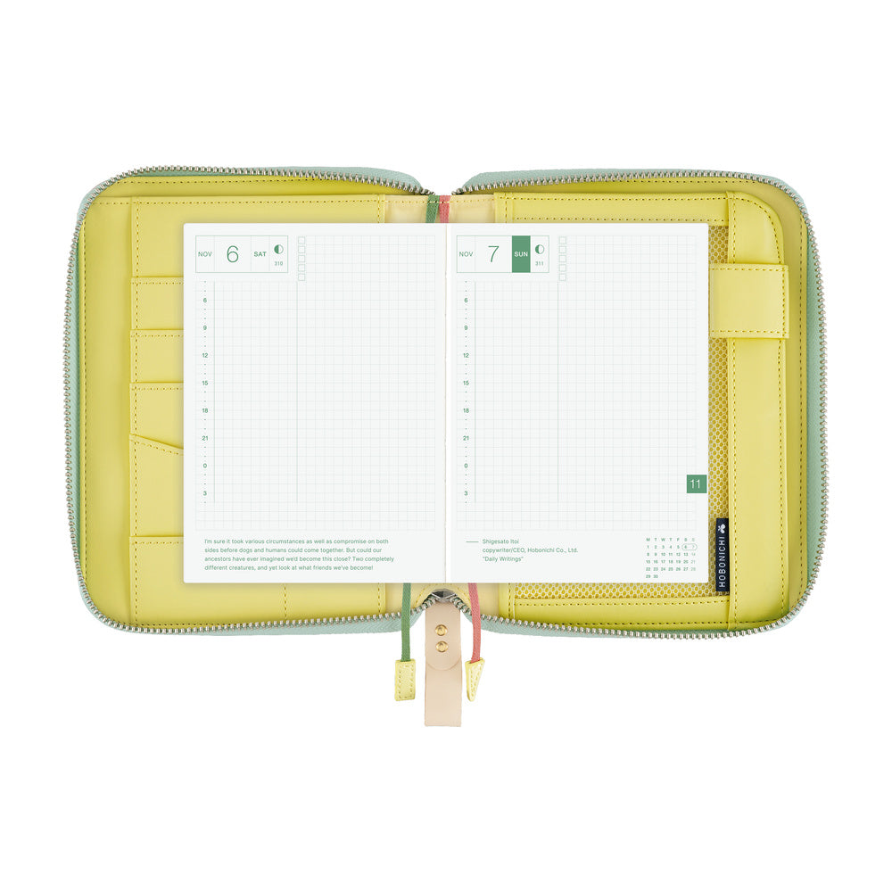 Open Hobonichi A6 zippered cover with yellow interior, card slots and pen loop, showing grid planner pages