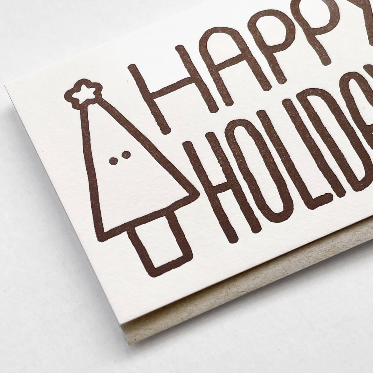 Close-up of the letterpress card showing a brown fir tree with a star and "Happy Holidays" lettering.