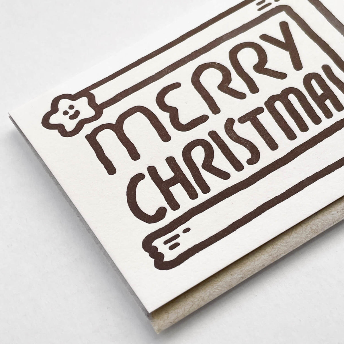 Close-up of the letterpress card showing brown "Merry Christmas" lettering and star, envelope tucked behind.