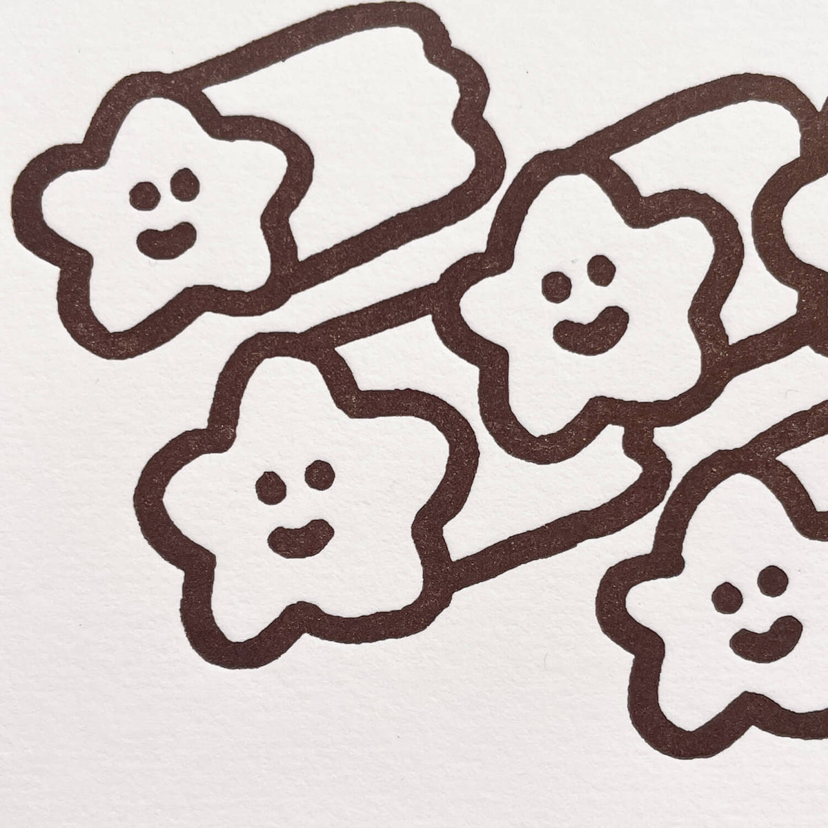 Close-up of letterpress printed smiling shooting stars in dark brown ink on textured white cotton paper.
