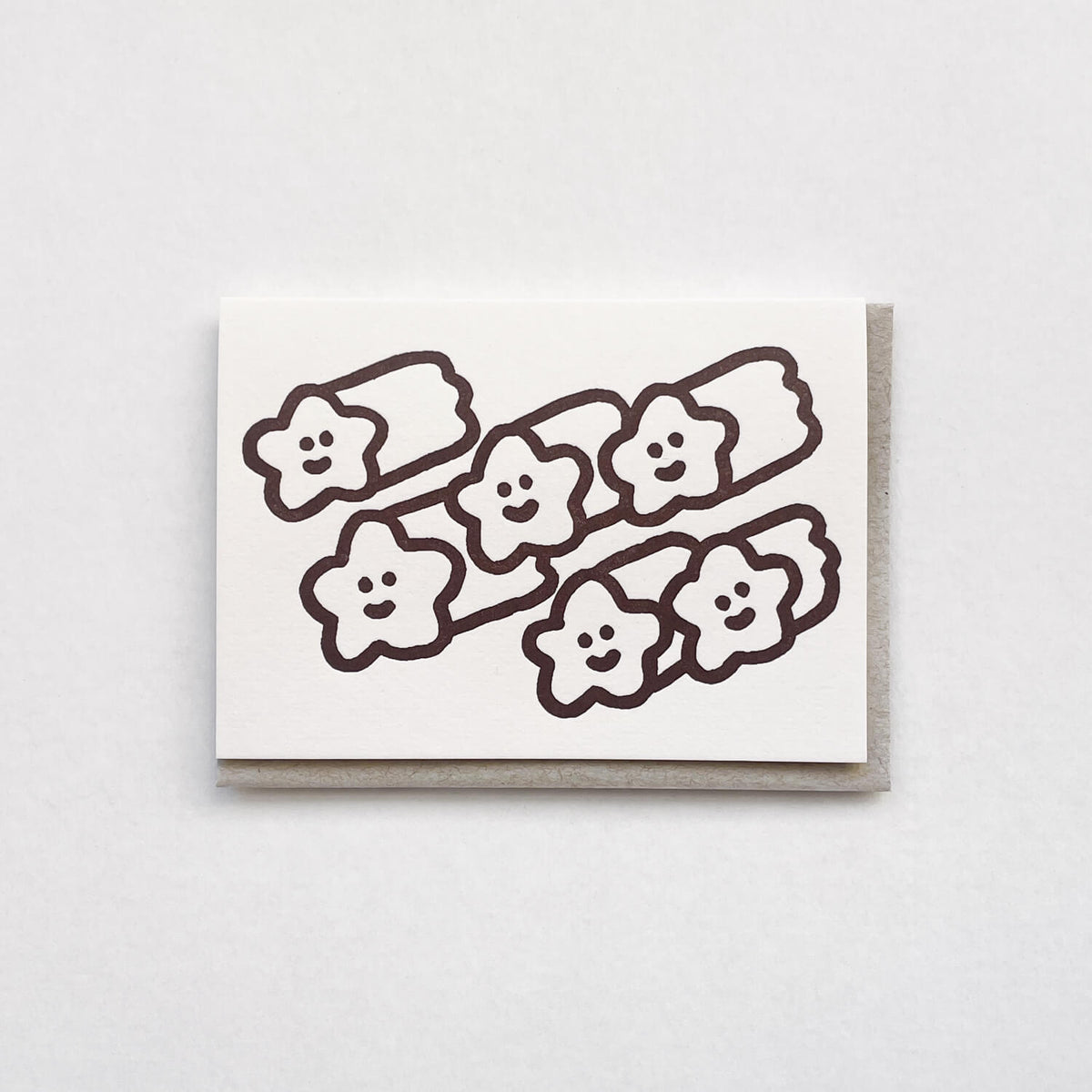 White letterpress card printed with smiling shooting stars in dark brown, on a grey envelope.
