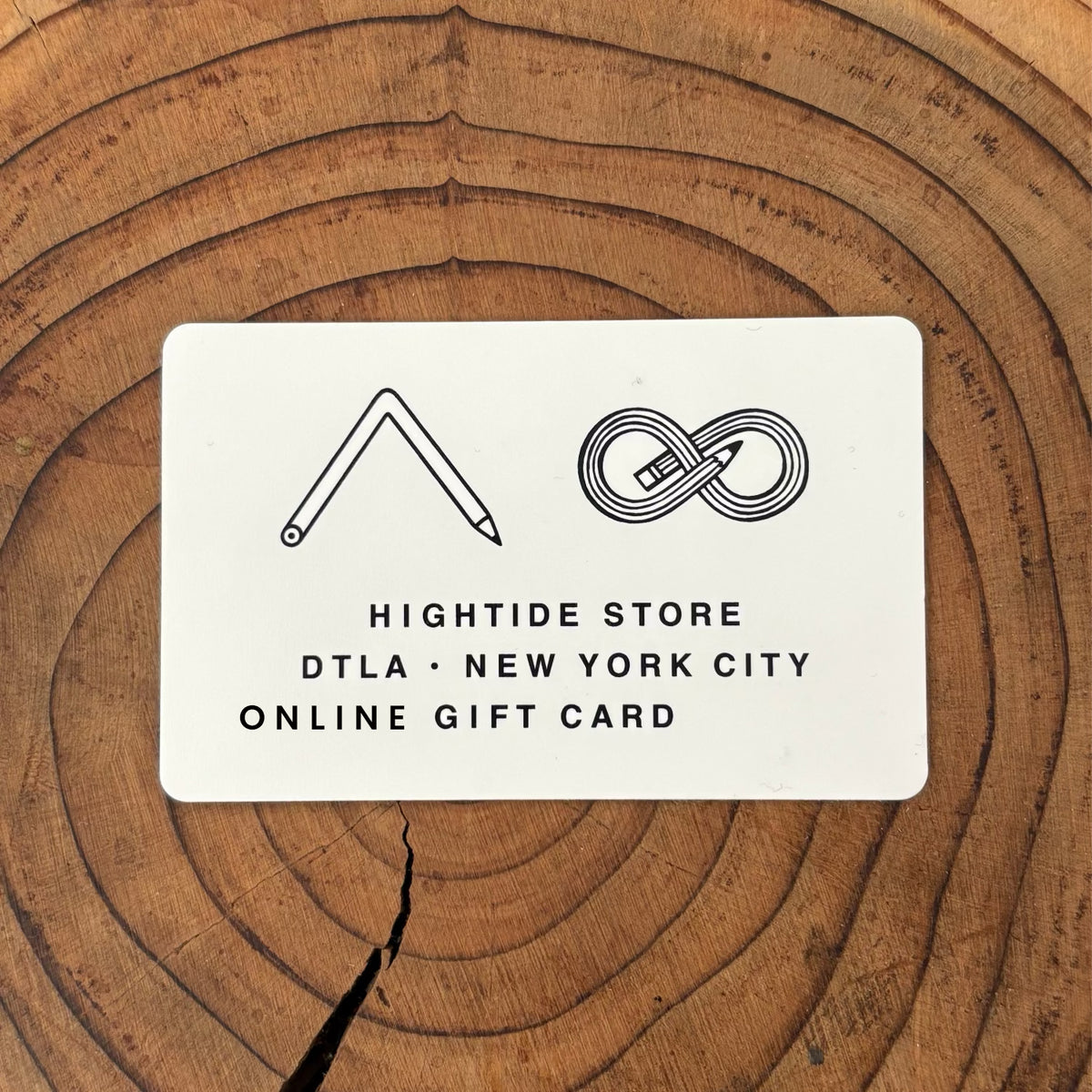 White HIGHTIDE Store online gift card with pencil logos, resting on a tree stump surface.