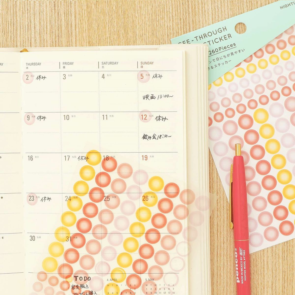 Yellow, orange and pink see-through dot stickers applied to an open planner, with sticker sheet and red pen alongside.