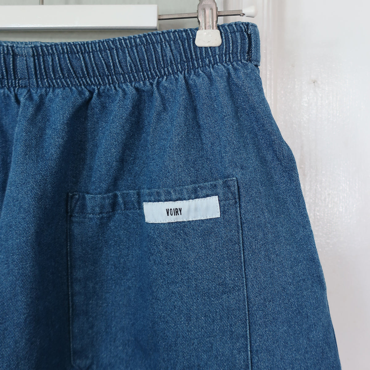 Close-up of Mid Blue denim pants showing the elastic waistband and patch pocket with a Voiry label.