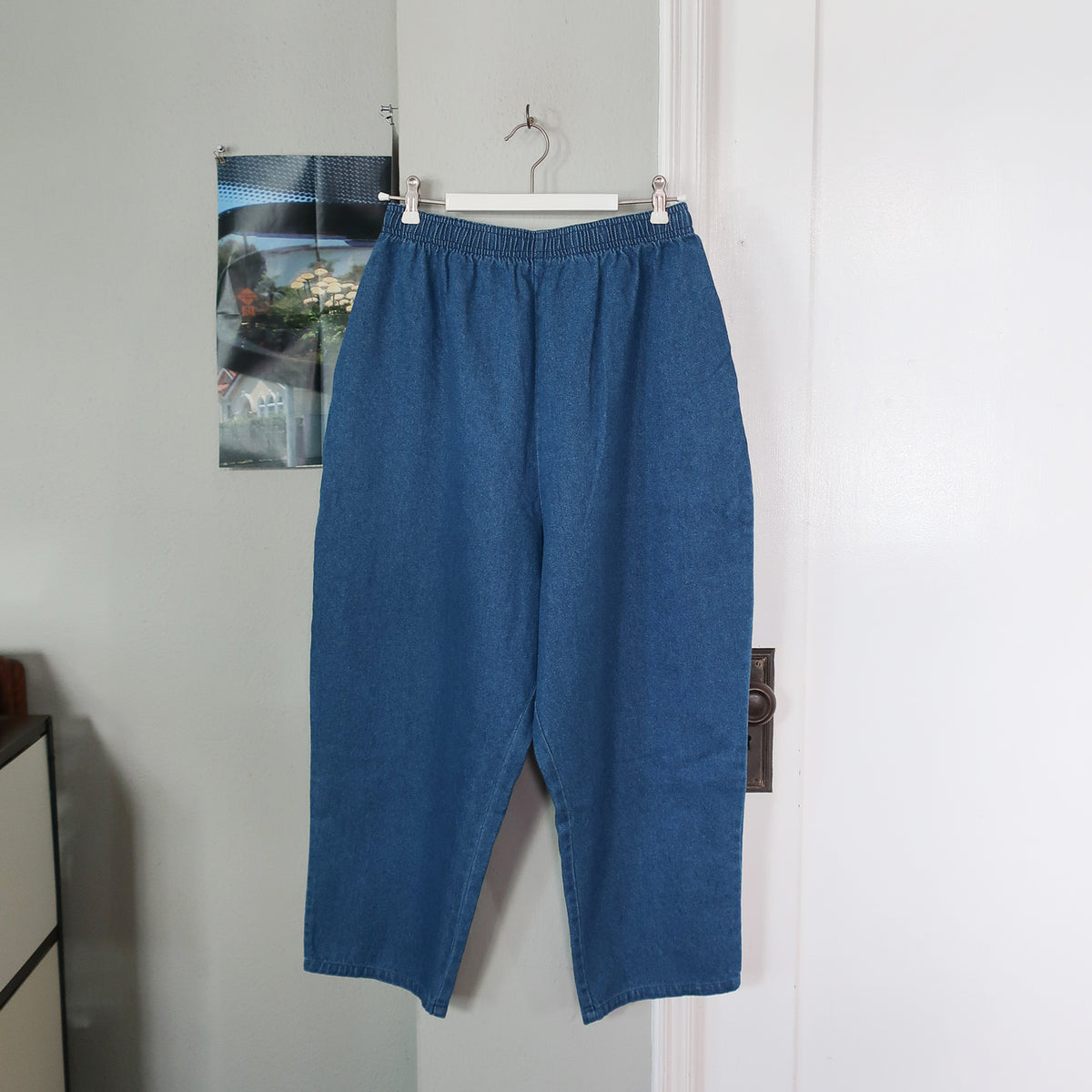 Voiry Sunday Pants in Mid Blue denim, elastic waist and side pockets, hung on a hanger on a door