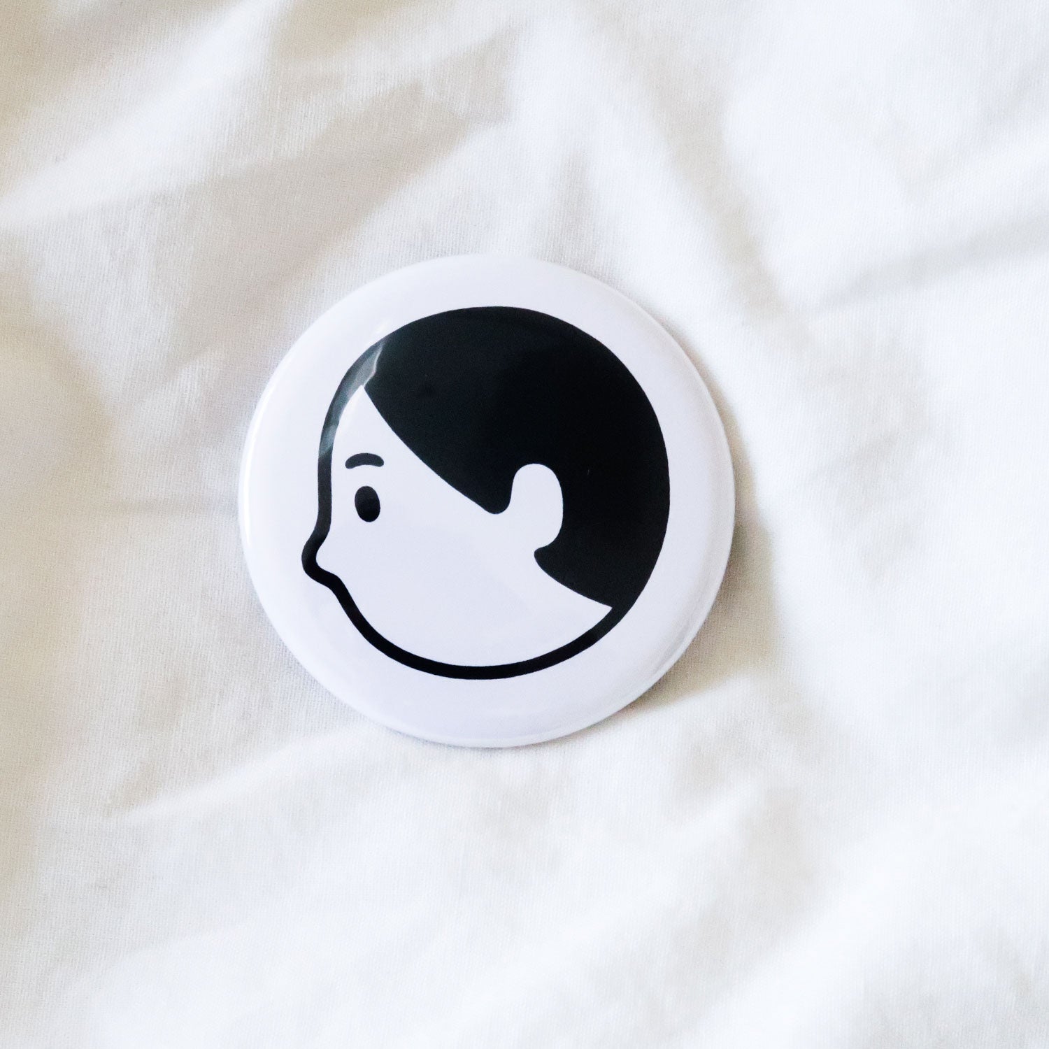 Round white pin badge printed with a black and white line drawing of a face in profile, on white fabric.