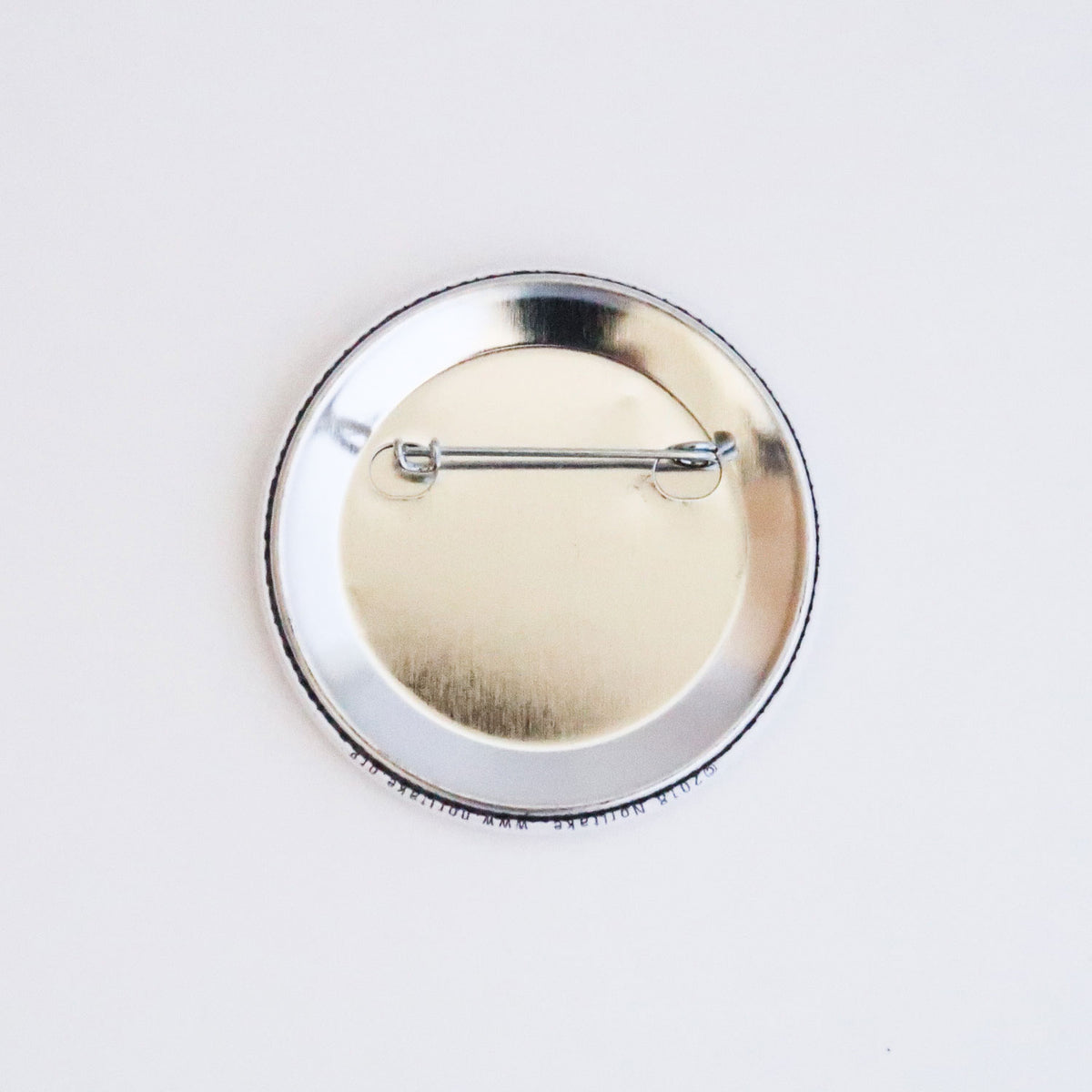 Back of the round Noritake pin badge, showing its silver metal casing and horizontal pin fastening.