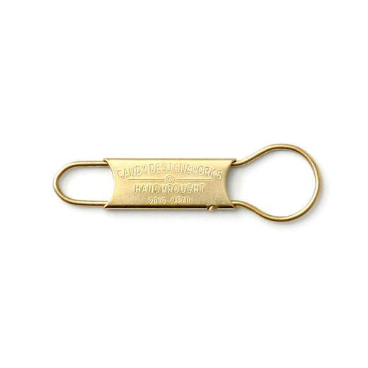 Brass key ring with a flat center plate stamped "Candy Design & Works Handwrought" between two loops.