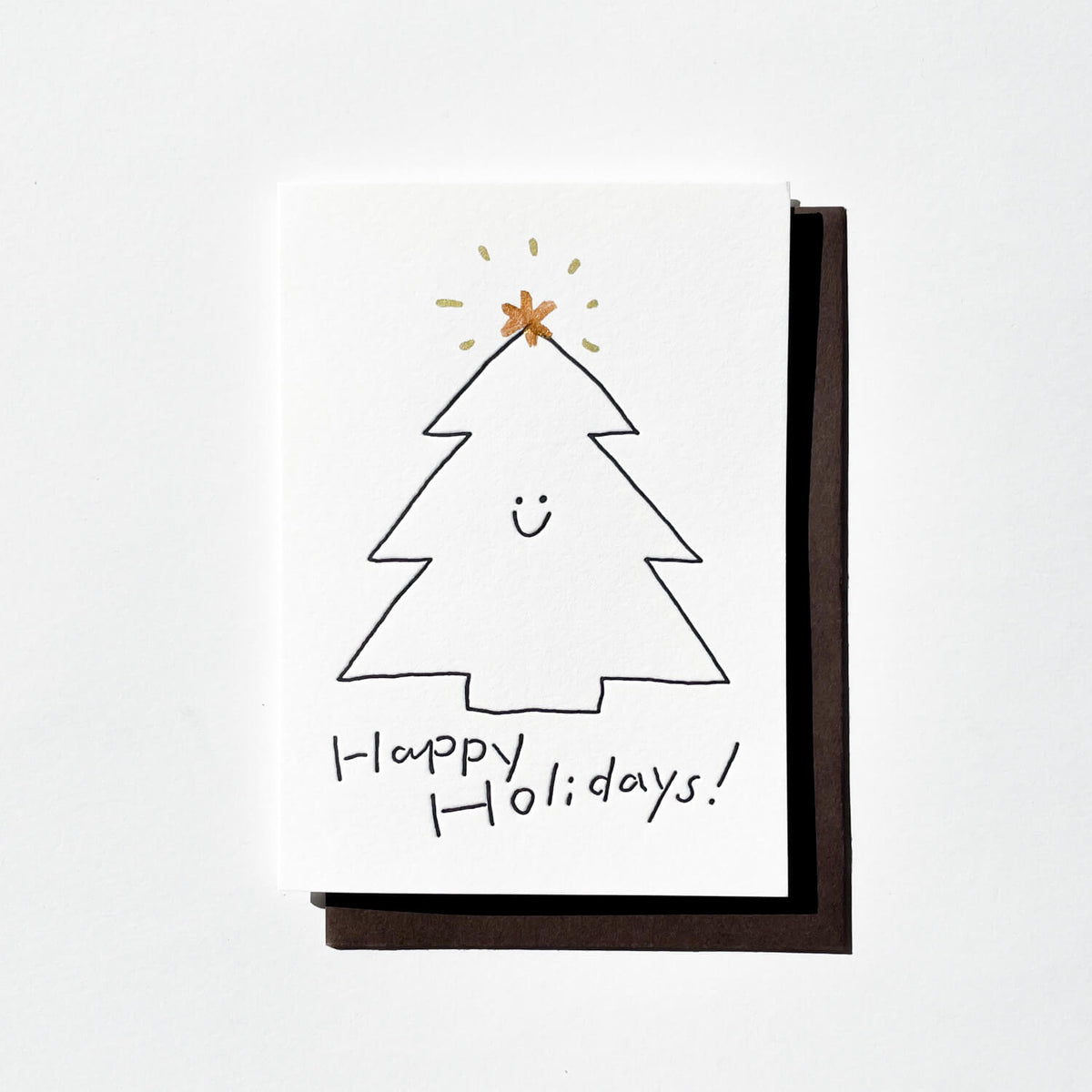 White letterpress card with a smiling Christmas tree, gold star and "Happy Holidays!", on a dark envelope.