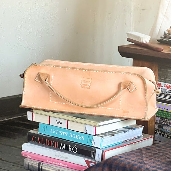Heritage Leather narrow mechanic tool bag in Natural leather with zipper closure, resting on a stack of art books.
