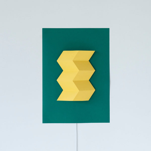 Sakaemark Poster Light with folded yellow zigzag paper on a green poster, mounted on a wall with cord