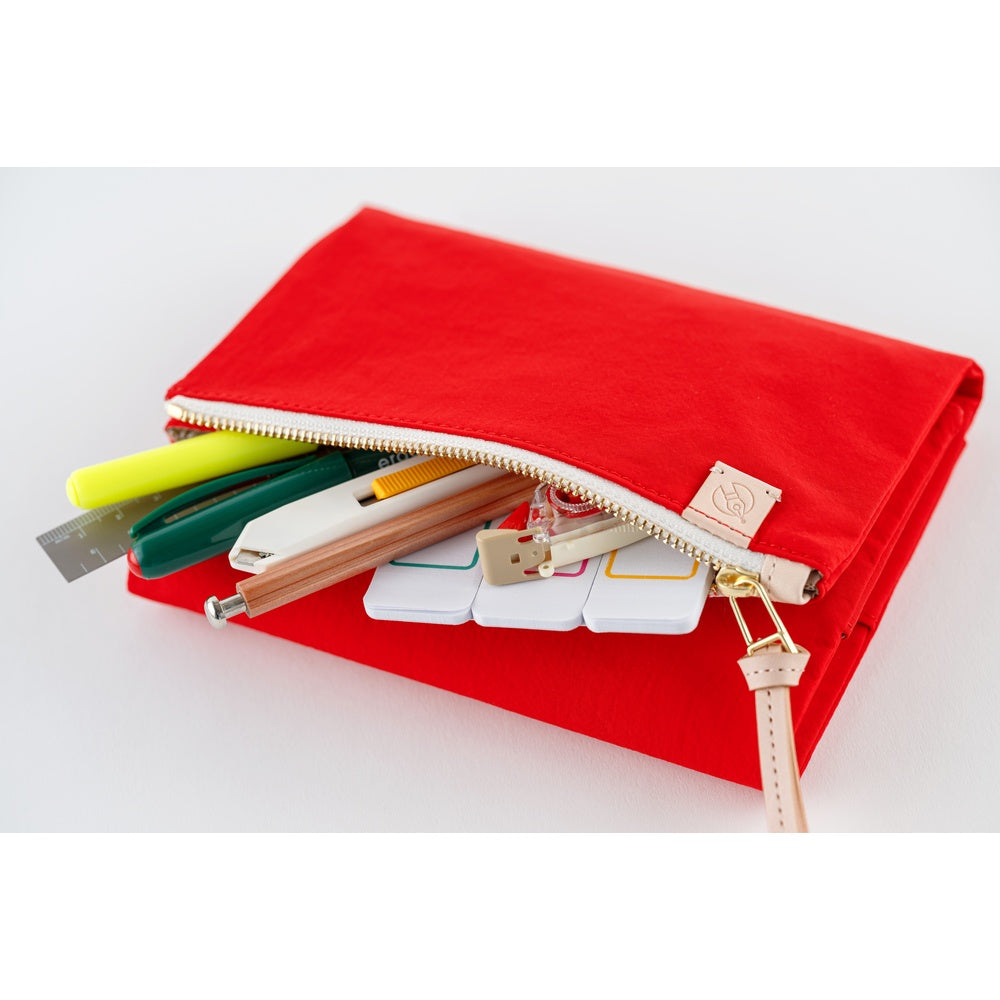 Red zippered Hobonichi book cover with leather wrist strap, holding pens, ruler, knife and sticky notes.