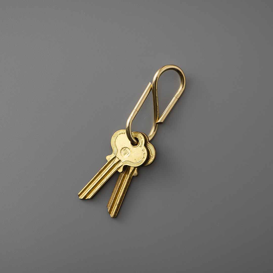 Brass S-shaped key ring holding two brass keys, shown on a plain grey background.