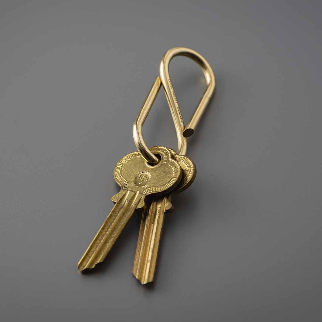 Brass S-shaped key ring holding two brass keys on a plain grey background.