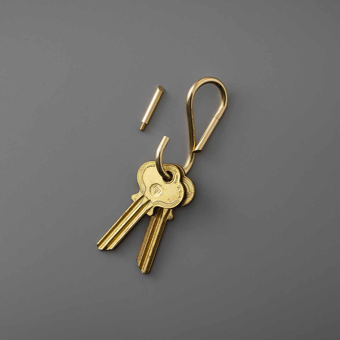 Brass hook-shaped key ring holding two keys, with its removable pin lying detached beside it.