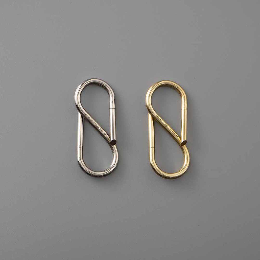 Two S-shaped metal key rings side by side in Nickel and Brass finishes on a grey background.