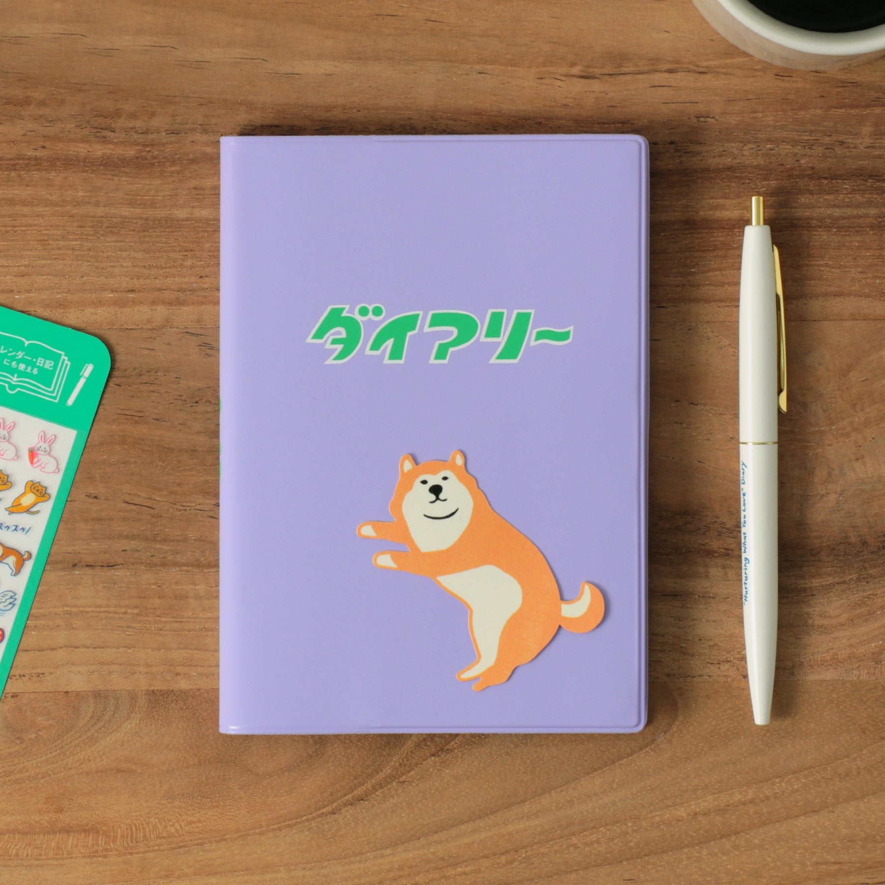 Purple A6 planner with Shiba-inu dog and ダイアリー on the cover, beside a white pen and sticker sheet.