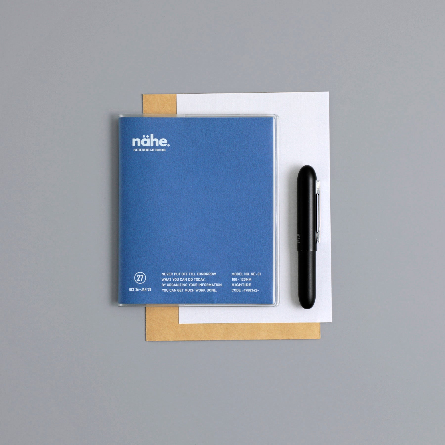 Nähe square monthly planner in Blue with clear cover, shown flat lay with white and kraft paper and a black pen.