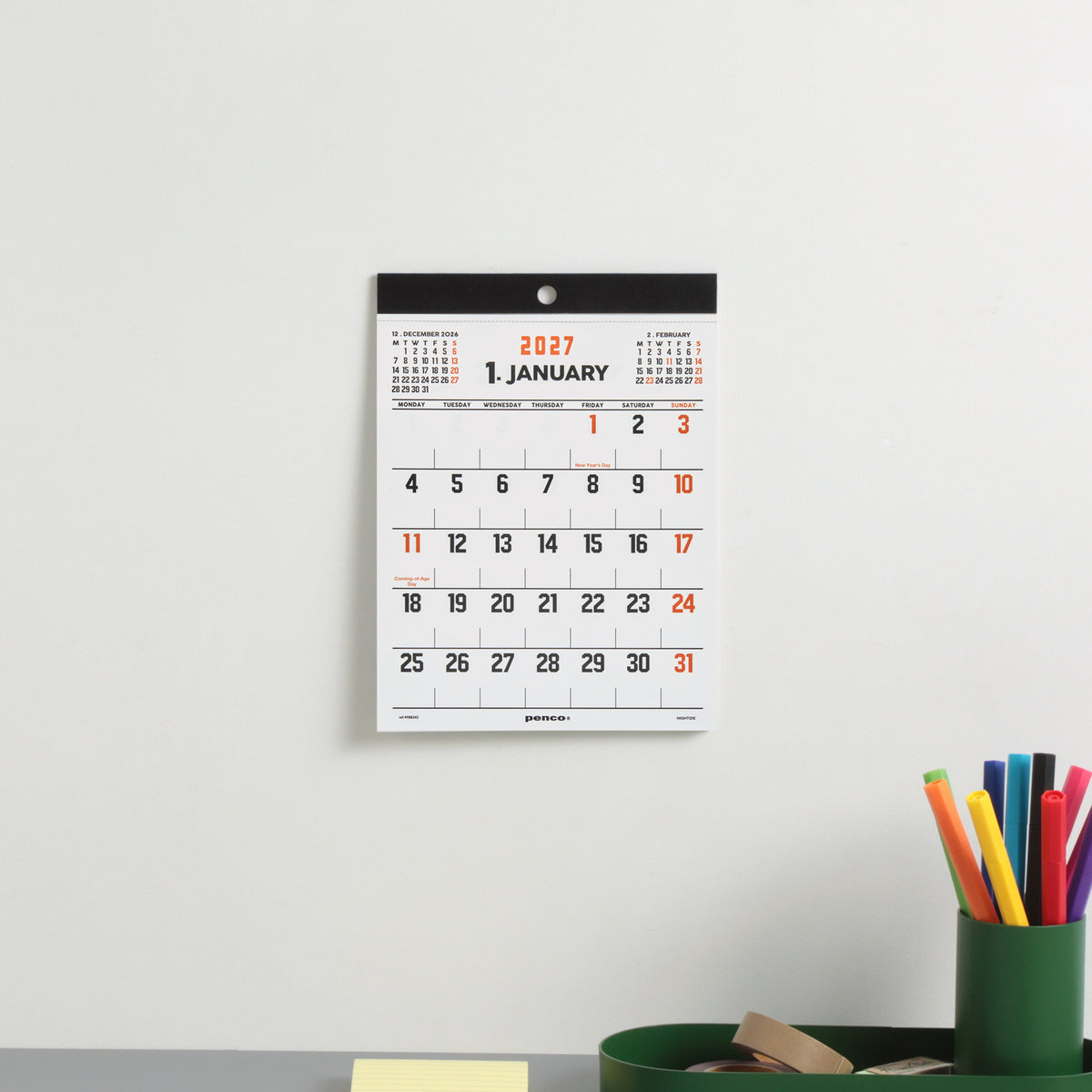 Penco A5 wall calendar hung on a white wall showing January 2027, above a green pen cup of markers.