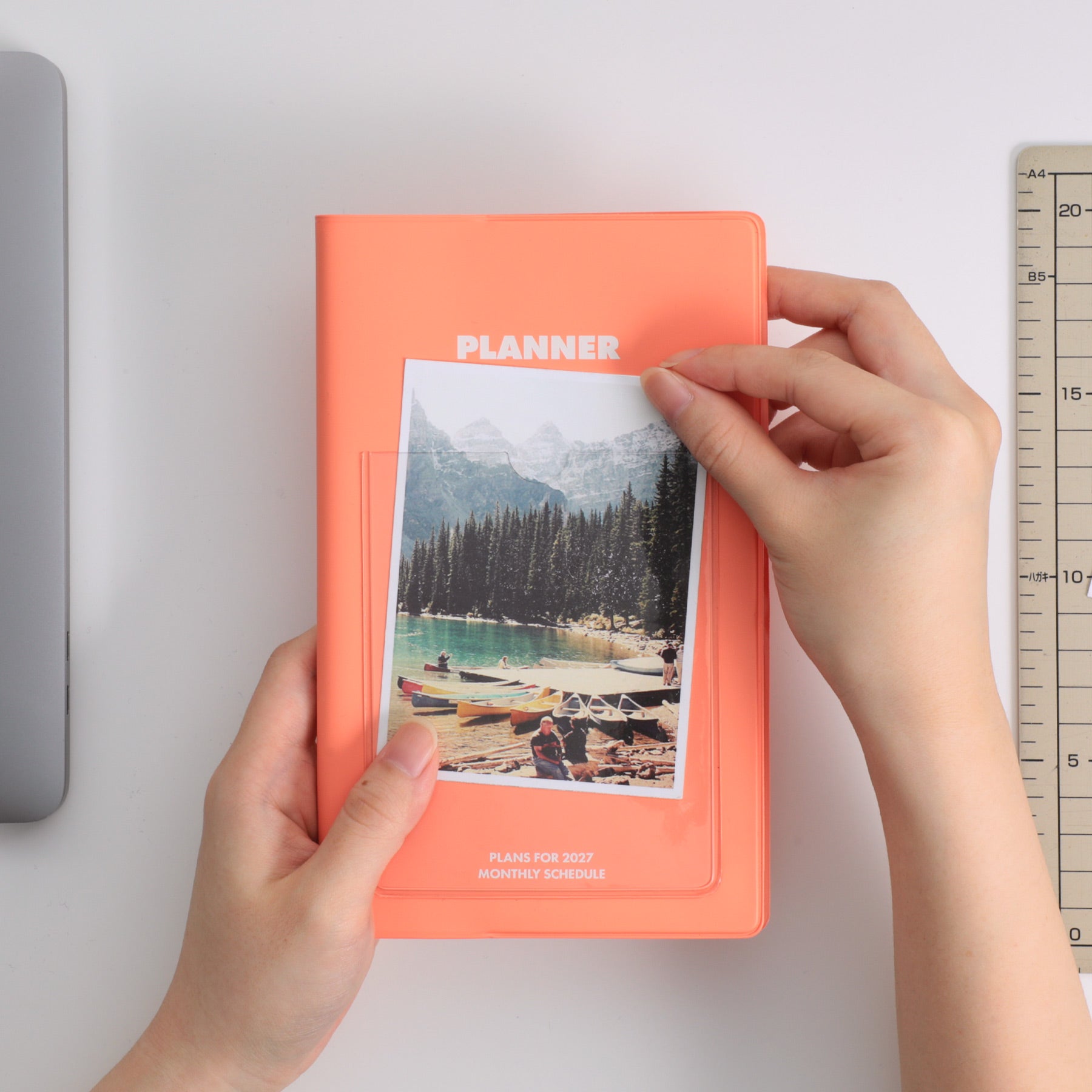Hands slipping a lake photo into the front pocket of a Pink Hightide Shine planner cover.