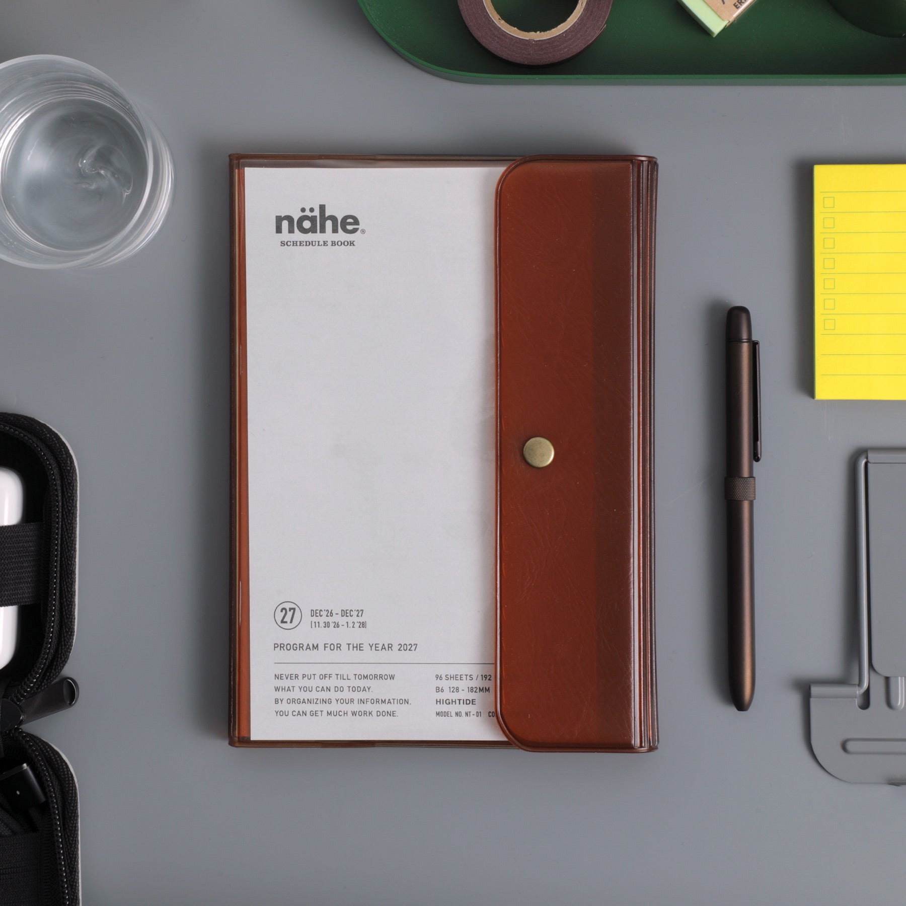 Nähe B6 weekly planner in Clear Brown cover with snap button, on a desk beside a pen and sticky notes.
