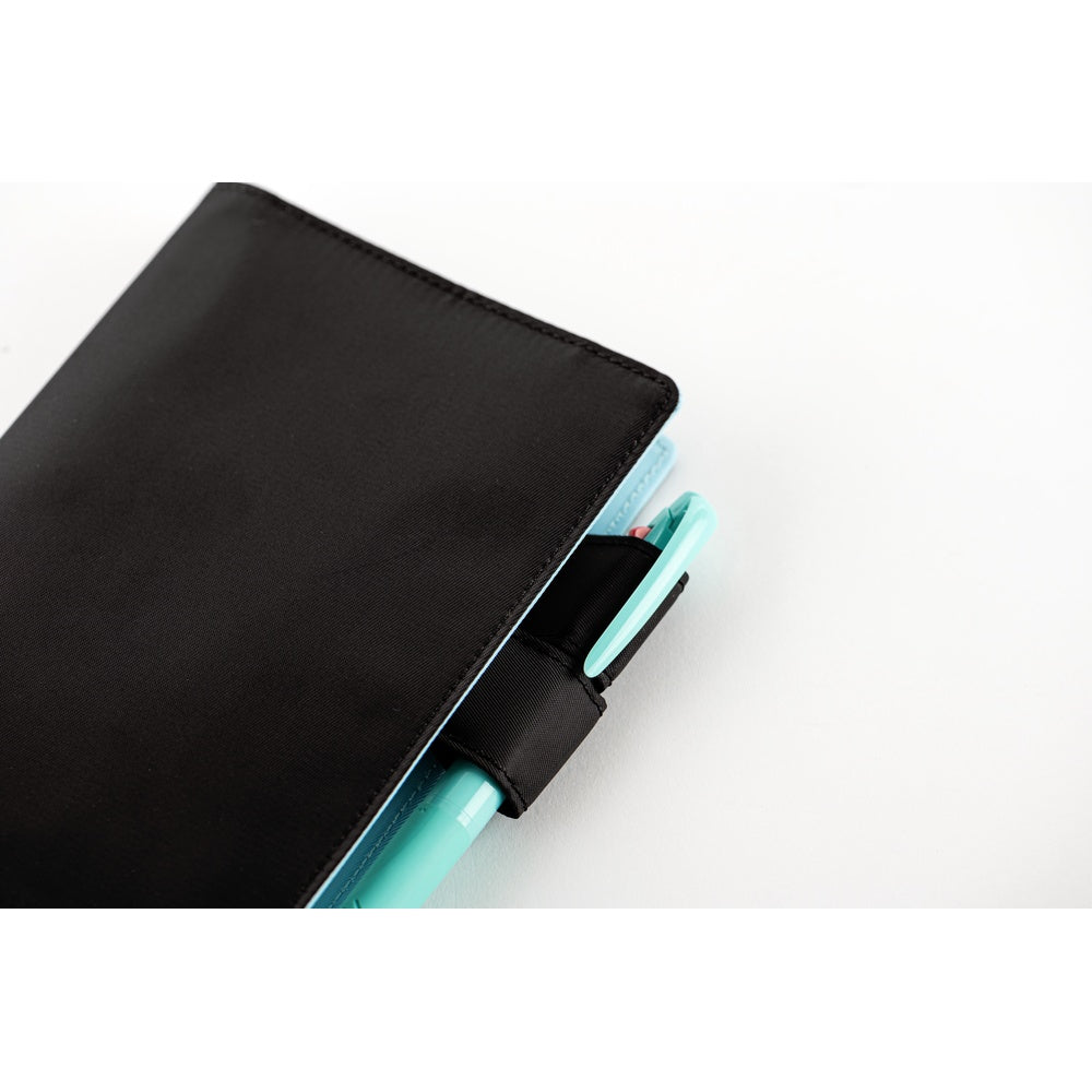 Close-up of the Black A6 cover's side pen loop holding a mint green pen alongside a planner