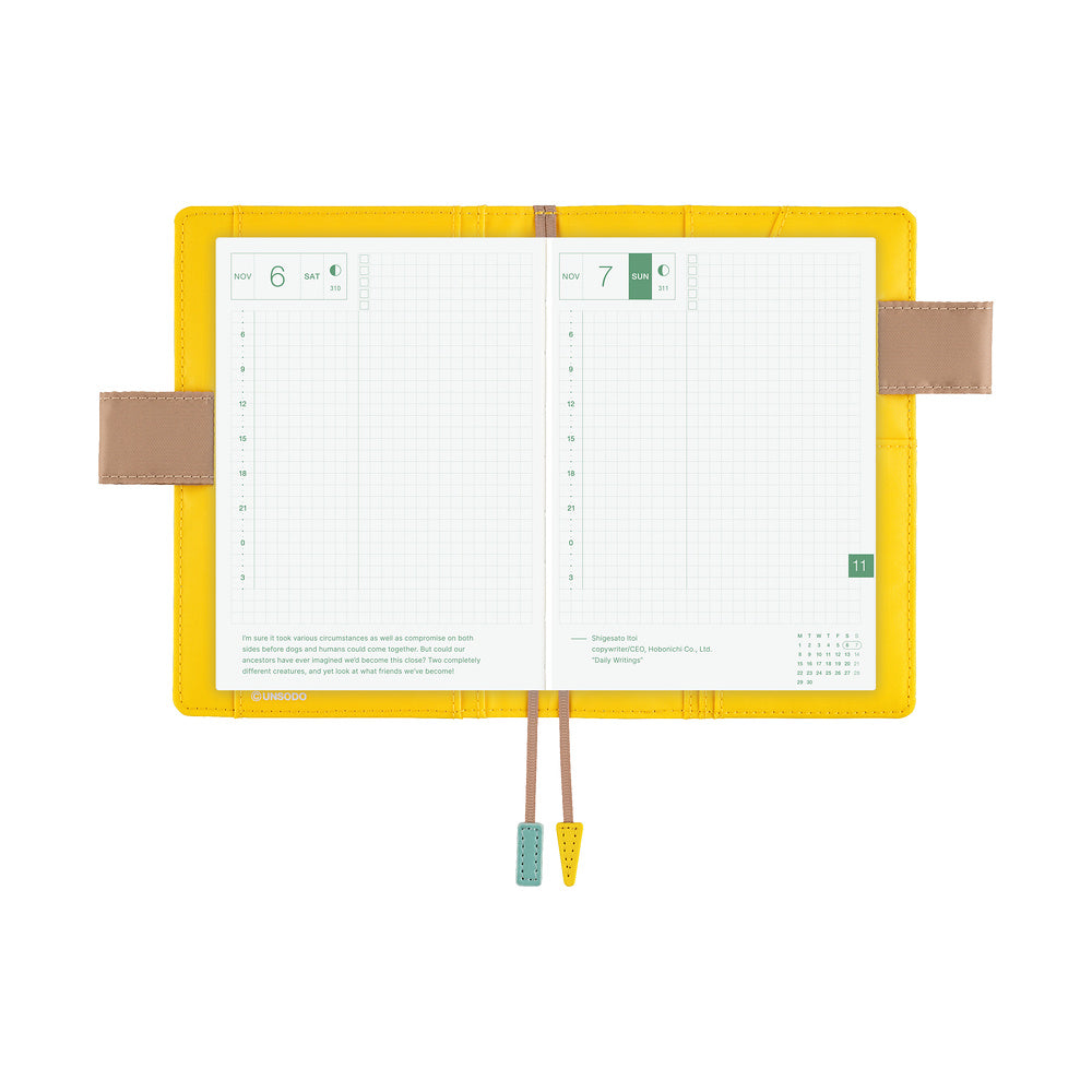 Yellow A6 book cover opened flat to show grid daily planner pages, side pen holders and two bookmark tassels.