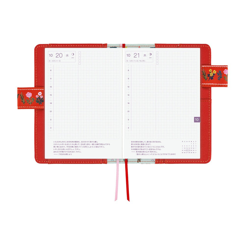 Red Hobonichi A6 book cover open flat, showing daily grid pages, embroidered floral side flaps and ribbon markers.