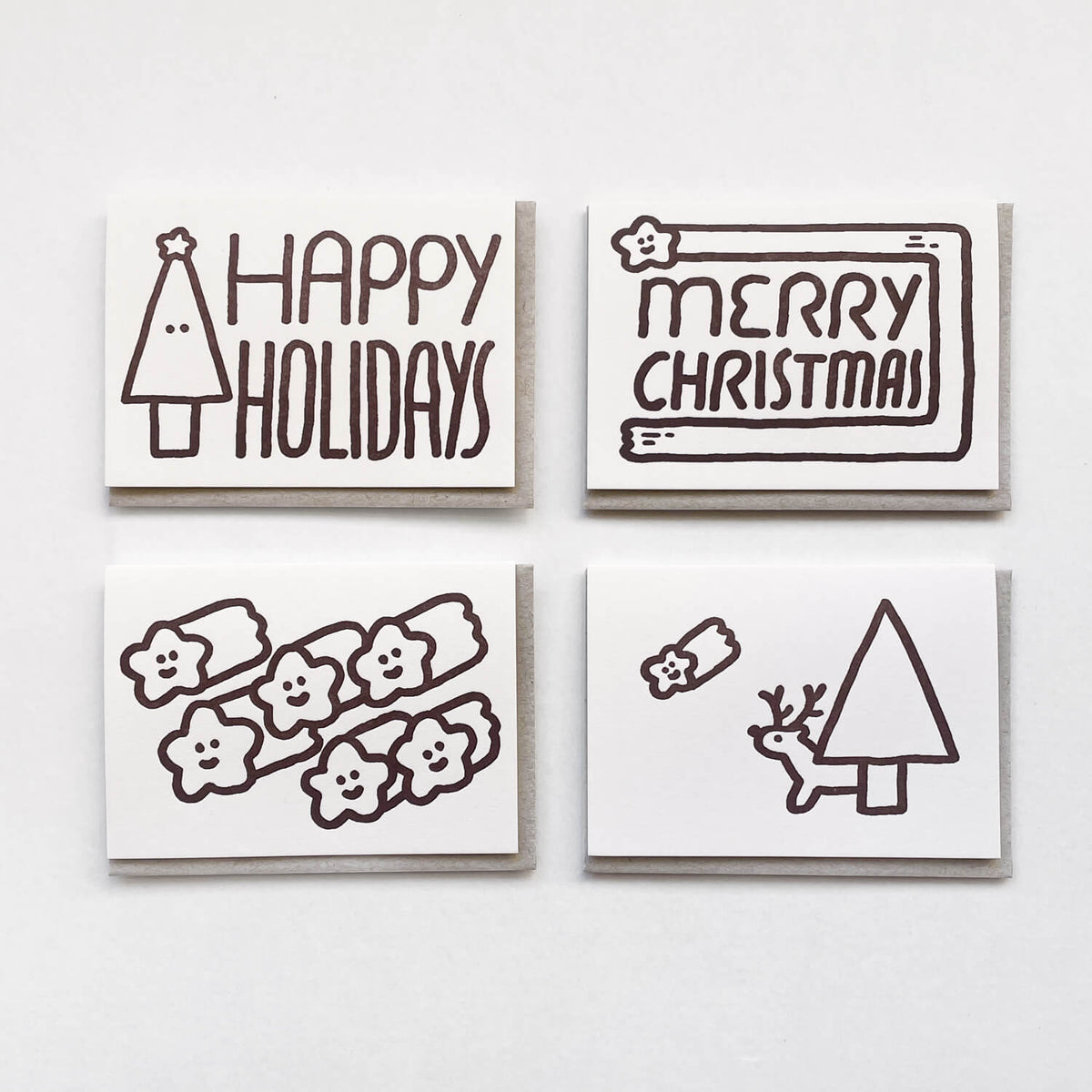 Four white letterpress cards with brown holiday drawings, including "Happy Holidays" and "Merry Christmas", on grey