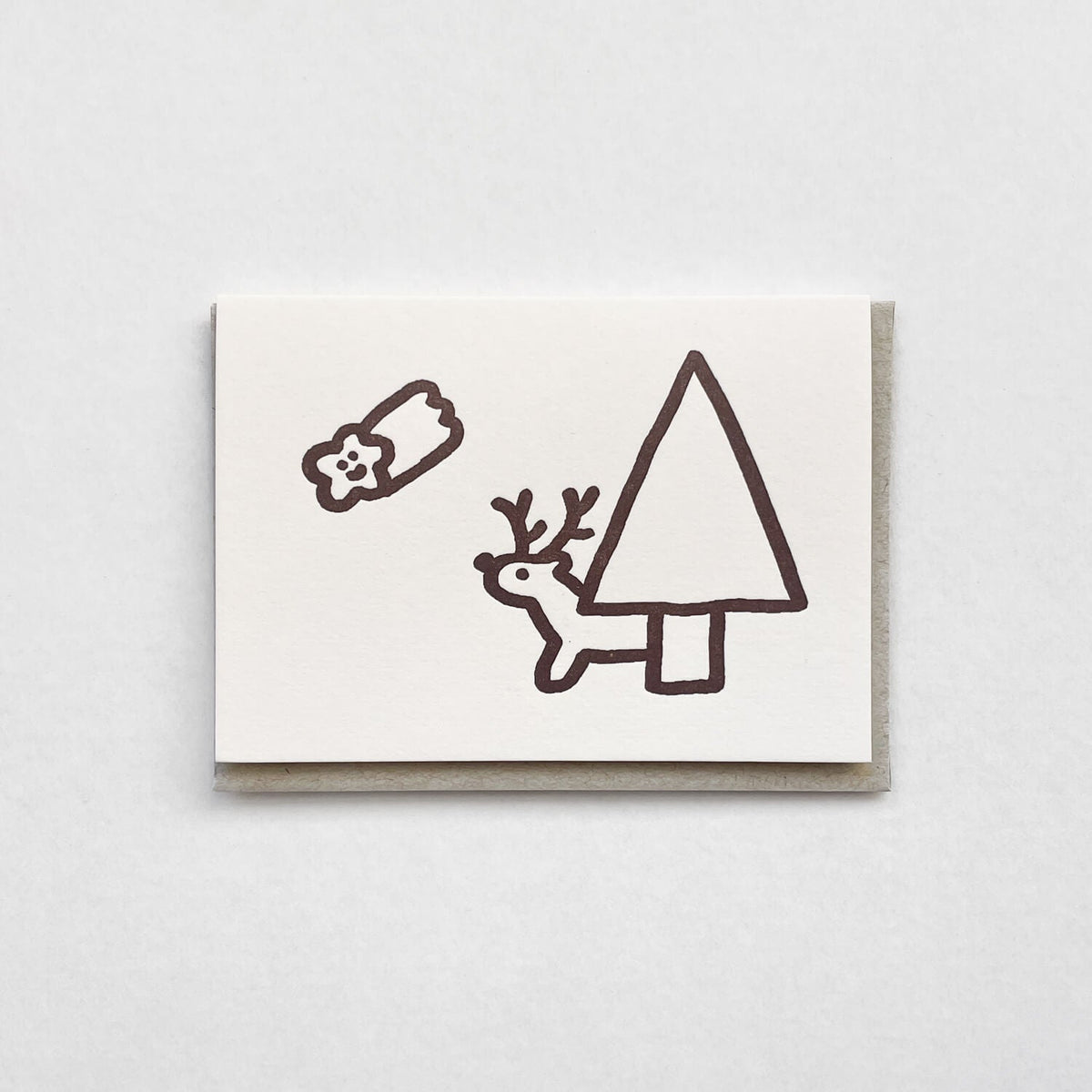 Letterpress card with a simple brown line drawing of a reindeer, tree and gift, on a grey envelope.