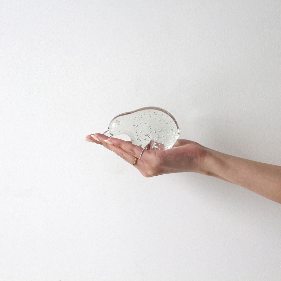 Open hand holding a small clear glass polar bear objet filled with tiny air bubbles, against a white wall.