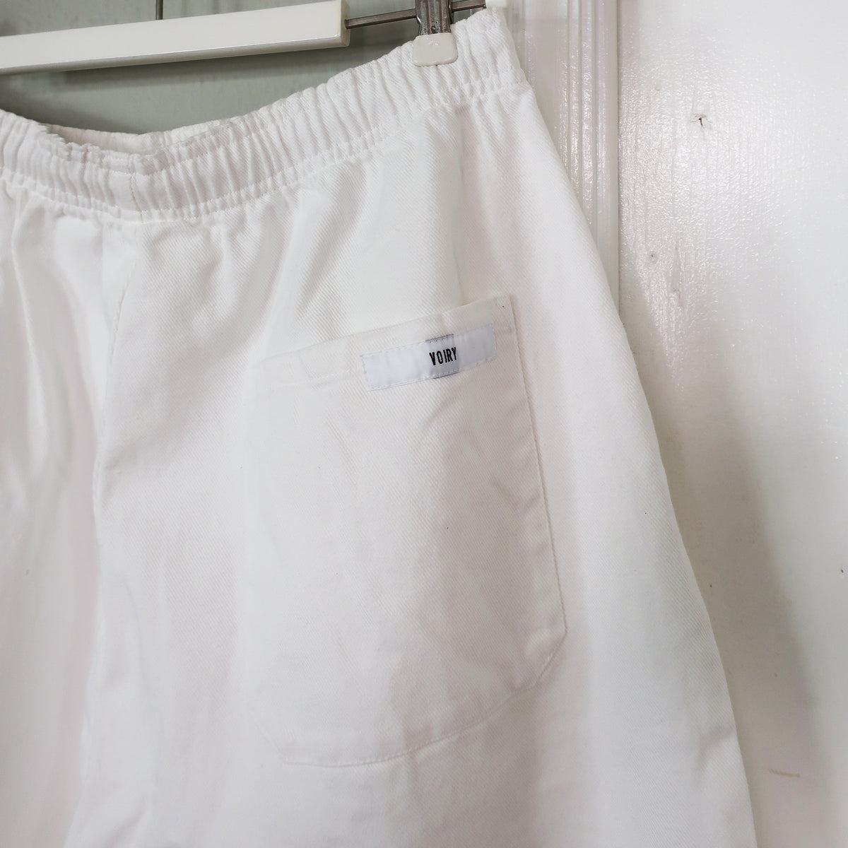 Close-up of Voiry Sunday Pants in White Denim, showing elastic waistband and patch pocket with brand label.