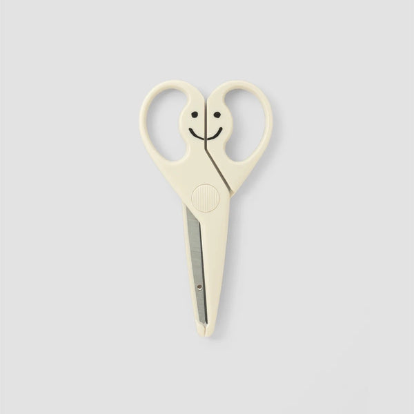 Cream-colored kids' scissors with a smiley face formed by the closed loop handles and stainless blades.
