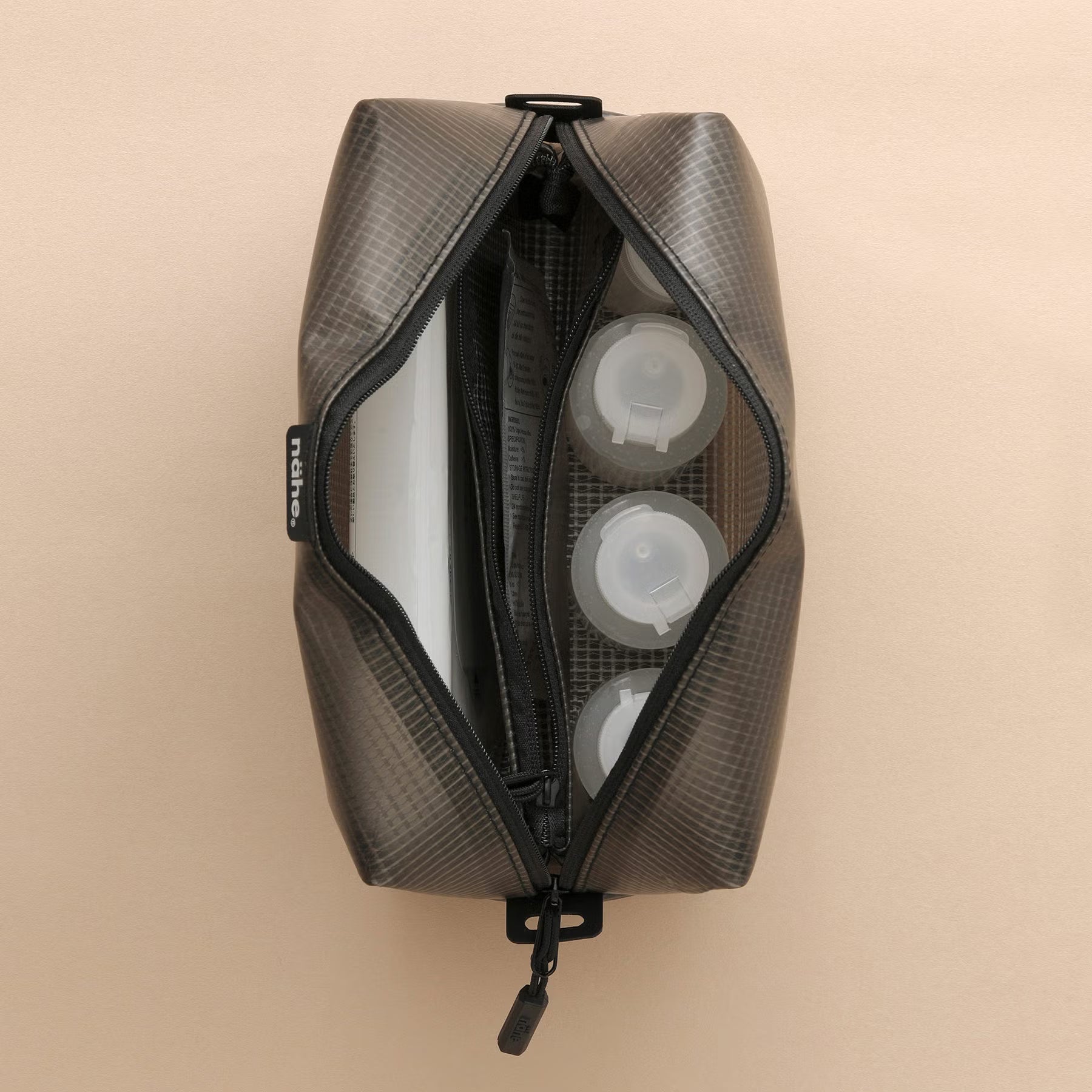 Nähe Soft Grid Pouch in Gray, unzipped to show toiletry bottles inside and a zippered internal divider.