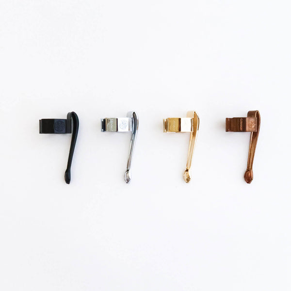 Four Kaweco slide-on pen clips lined up in Black, Chrome, Gold and Bronze Raw finishes, each engraved with the logo.