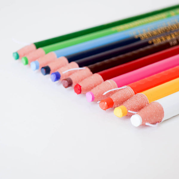 Close-up of Mitsubishi Dermatograph pencils lined up in a row, showing paper-wrapped tips with pull strings.